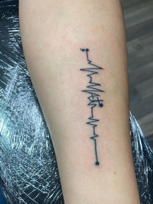 Heartbeat tattoo with letters on the bicep stands out