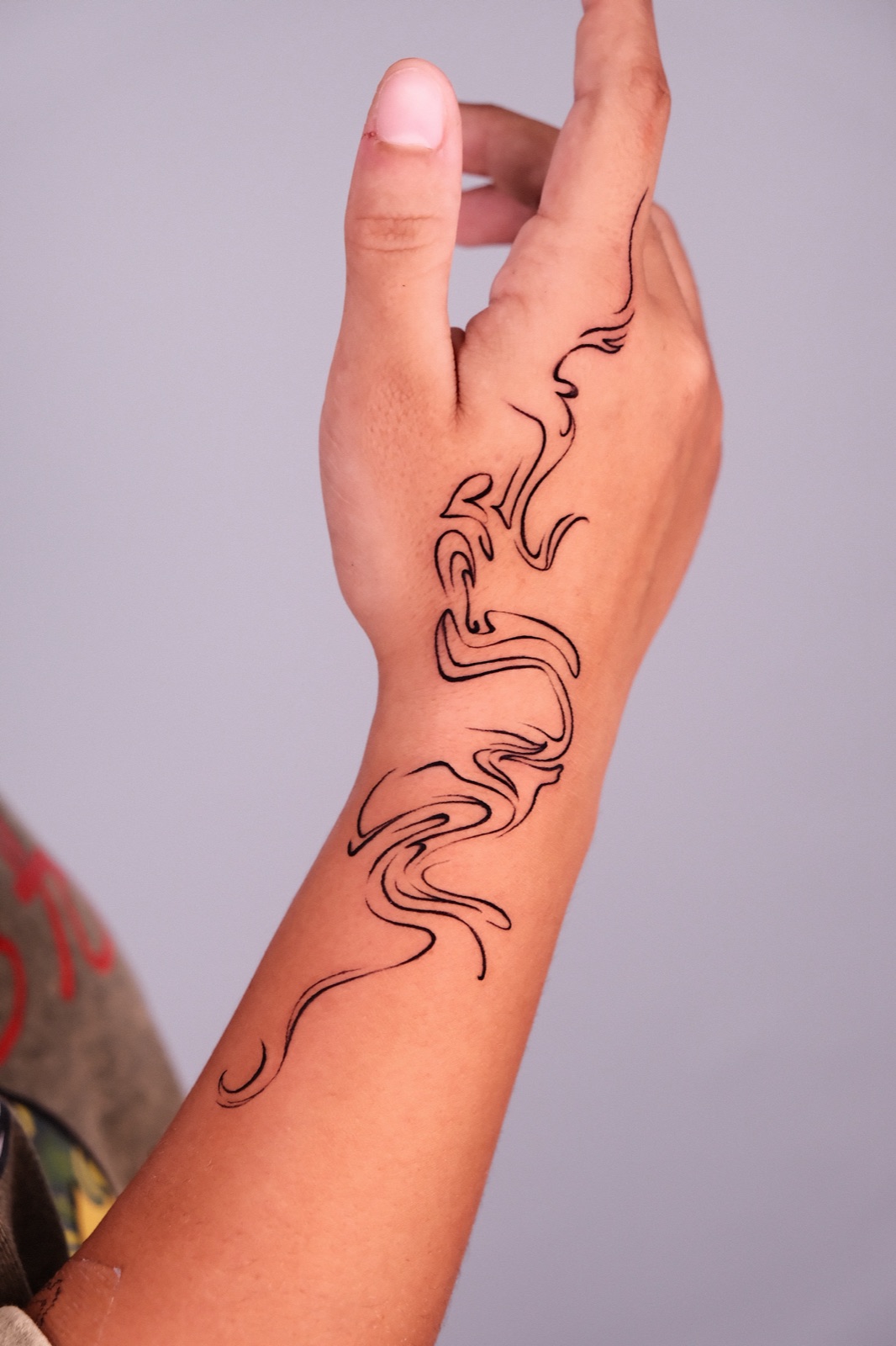 An abstract fine-line swirl tattoo flowing from the hand up the wrist