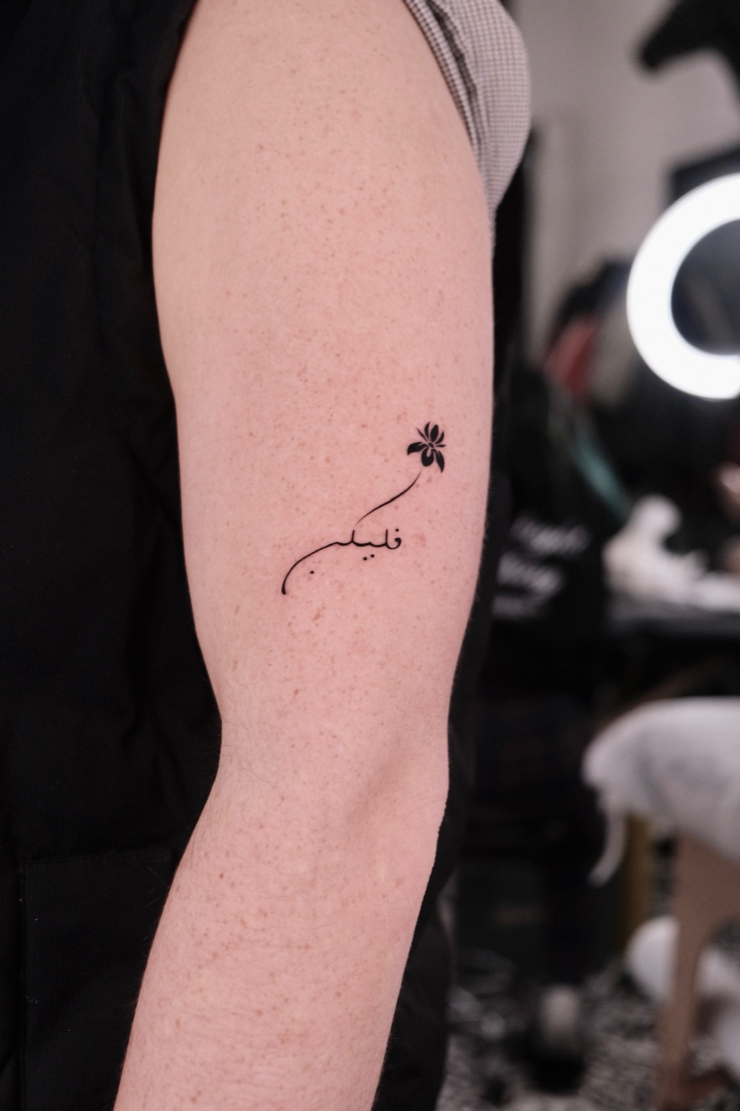 Arabic calligraphy lettering tattoo with a small flower on the upper arm