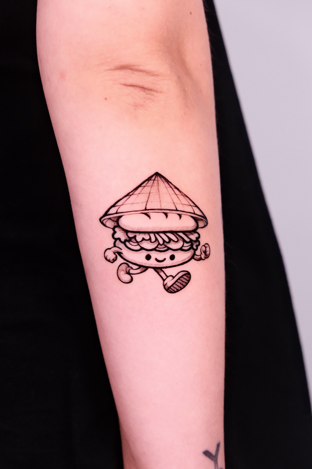 Cute walking banh mi sandwich mascot wearing a conical hat, tattooed on forearm at Sutran