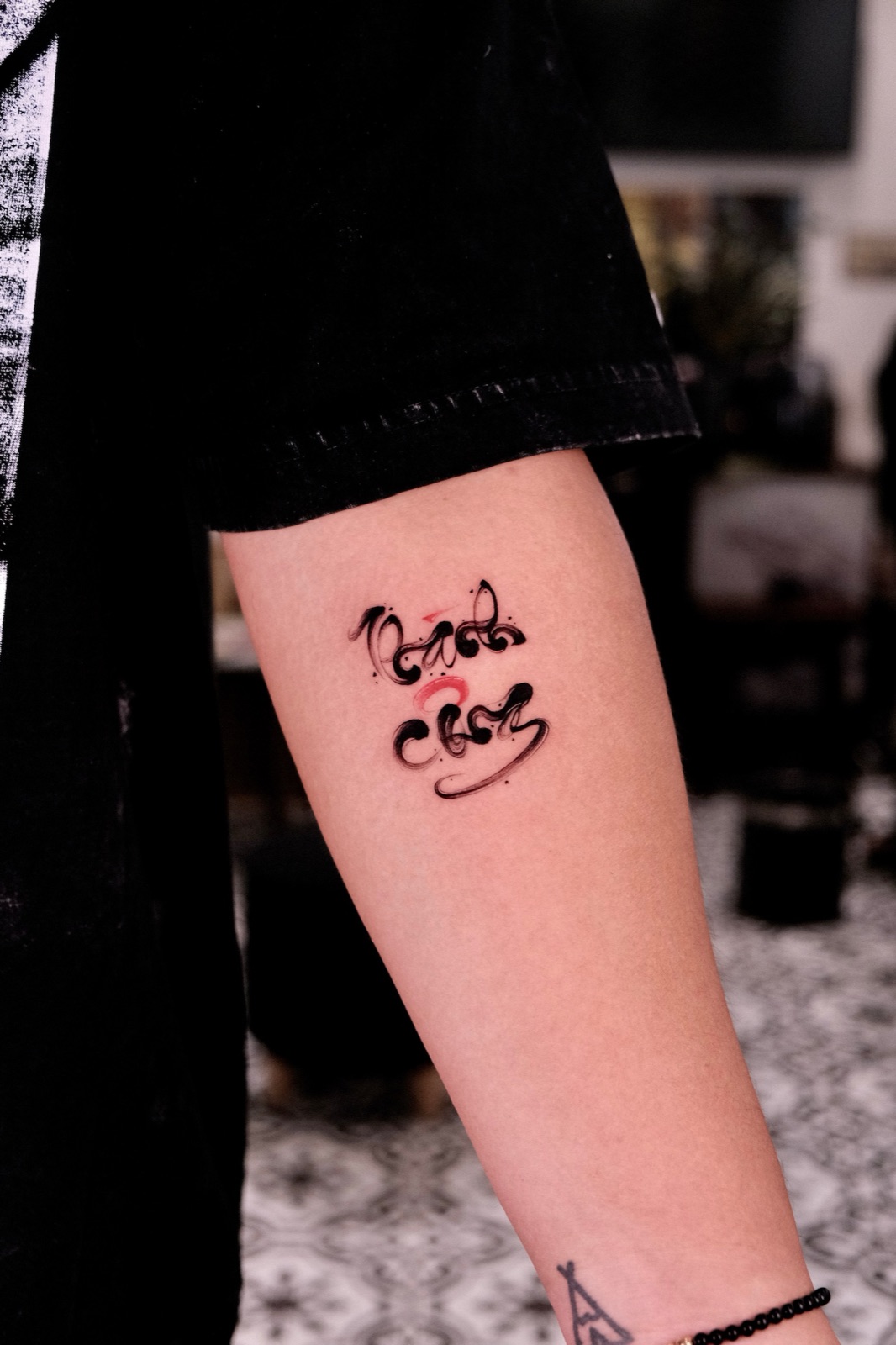 Brush calligraphy lettering tattoo in black and red on forearm