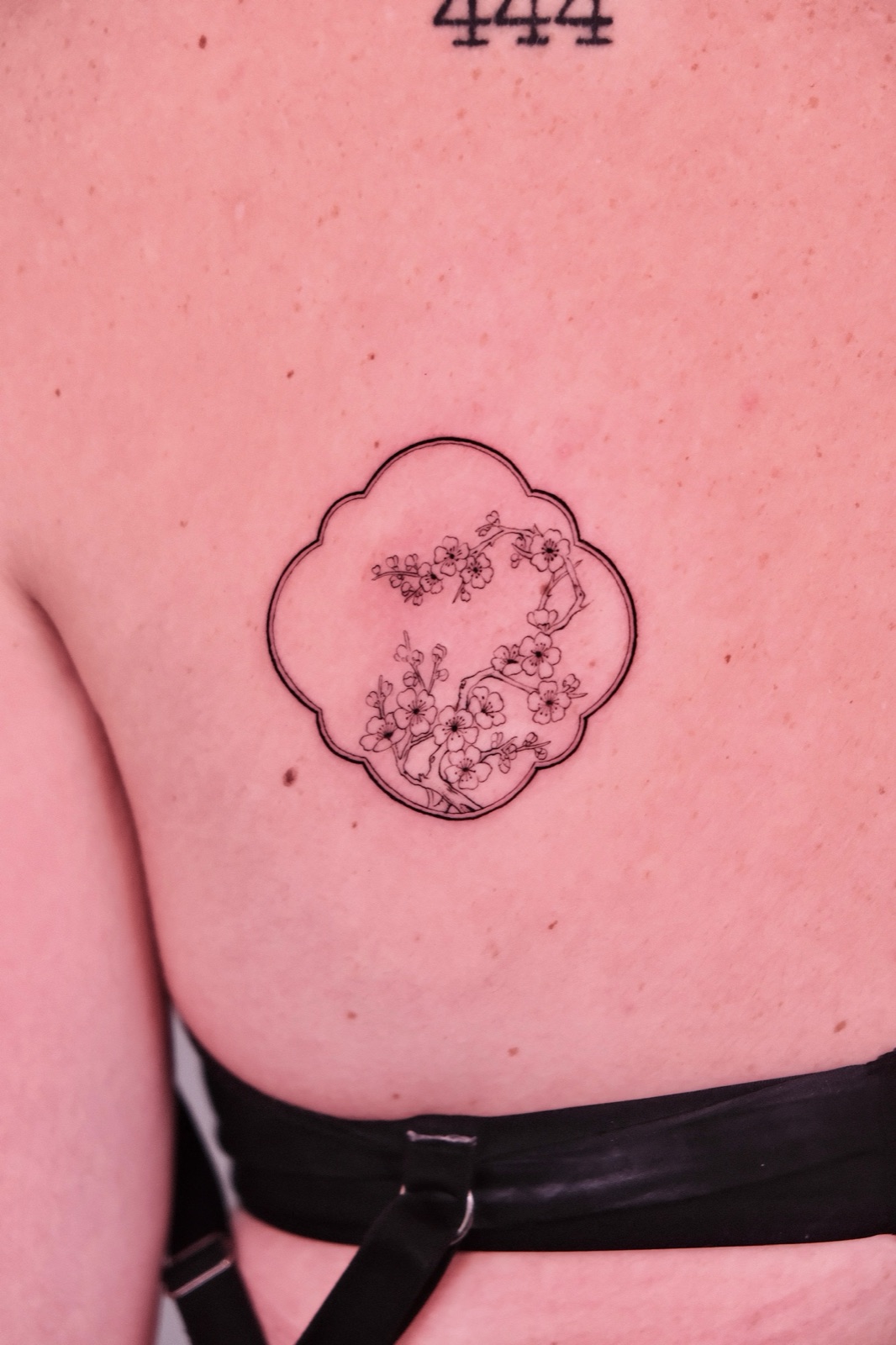 Fine line cherry blossom branch tattoo inside a quatrefoil frame on the chest