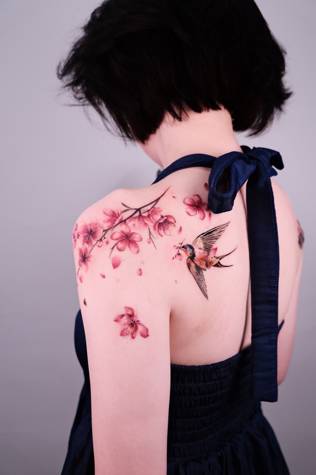 Colorful cherry blossom branch with a swallow bird tattoo on the shoulder blade