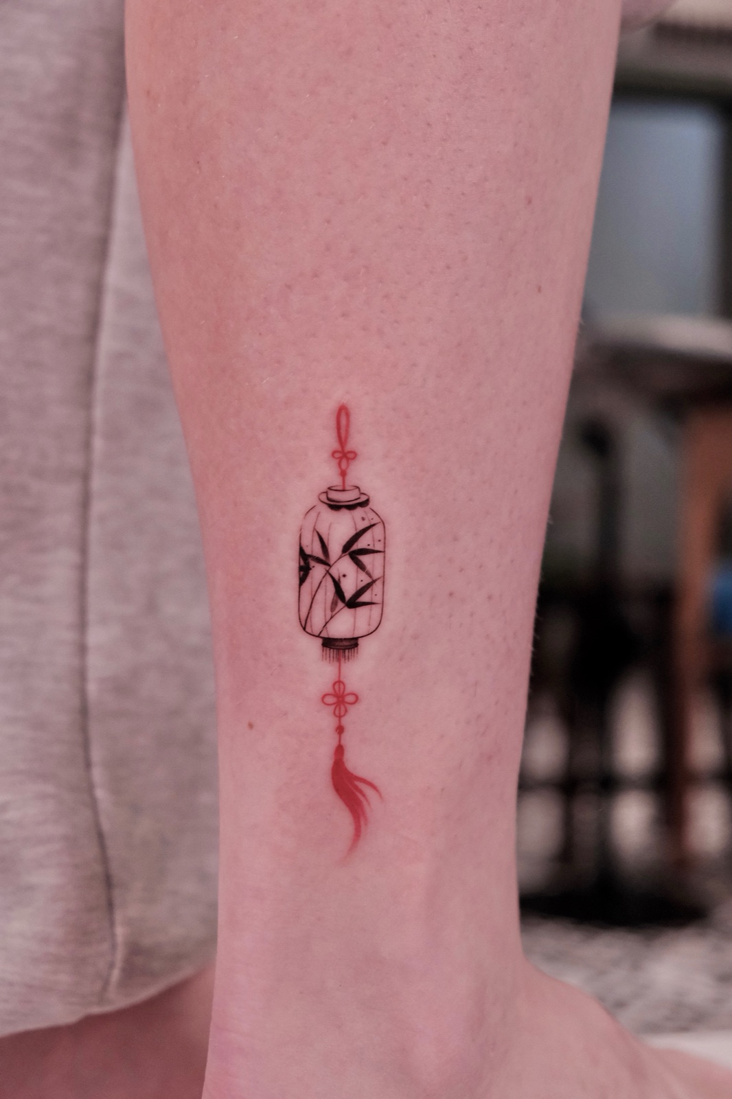 Lantern tattoo with bamboo leaves inside and a red tassel on the ankle