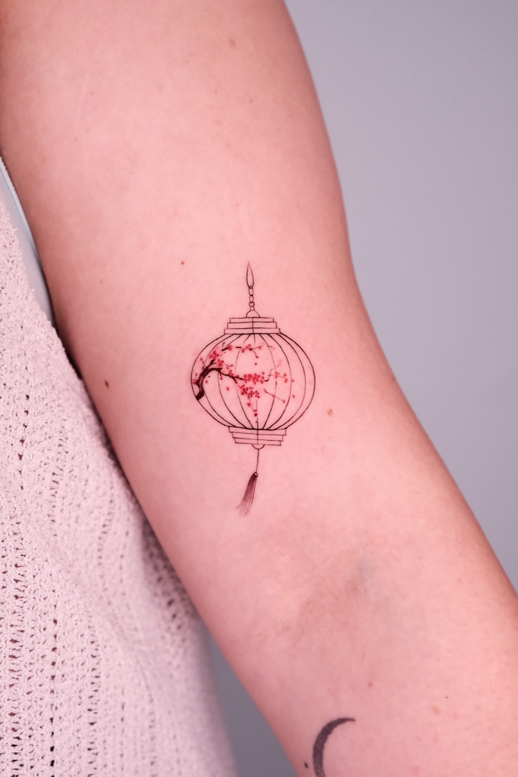 Fine-line Chinese lantern with a cherry blossom branch tattoo on the upper arm