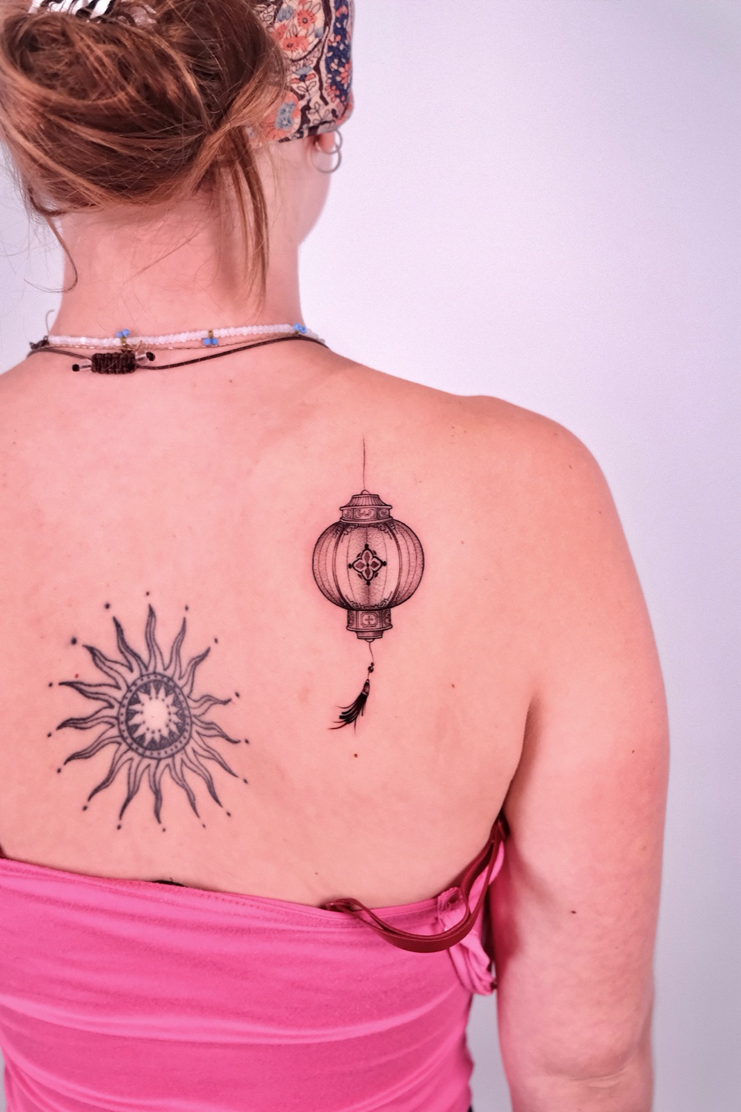 Fine-line Chinese lantern tattoo on shoulder blade beside a sun tattoo