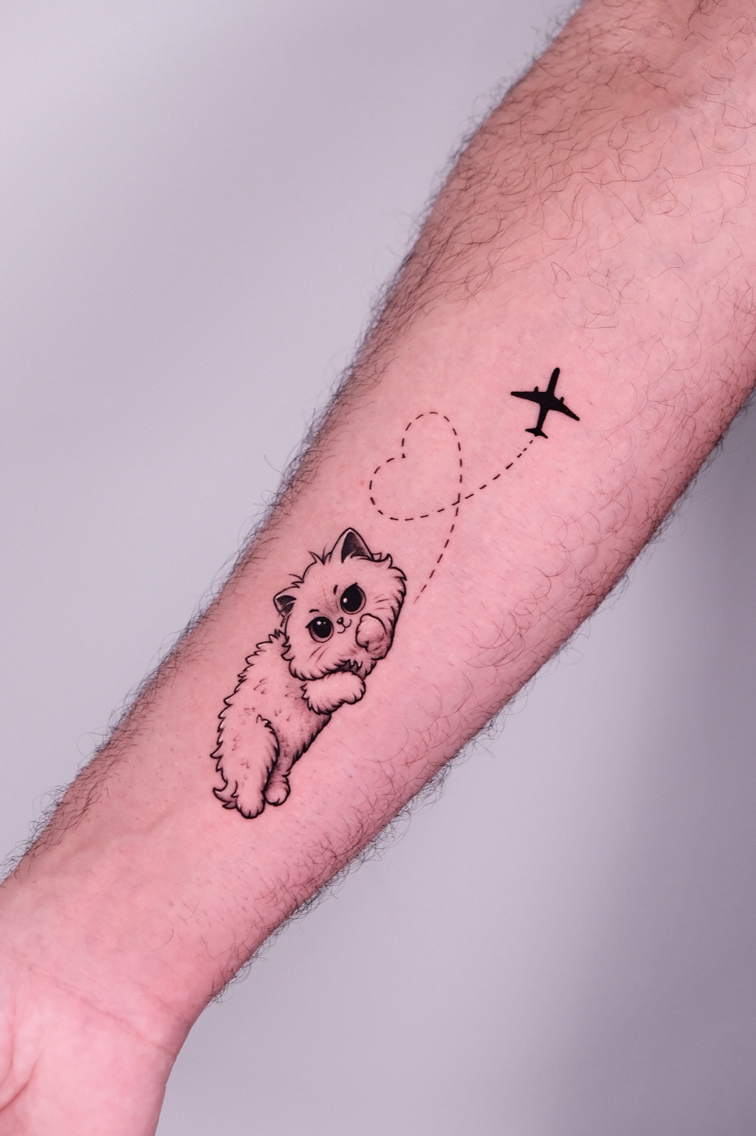 Tattoo of a fluffy cat with a heart-shaped flight path and airplane on forearm