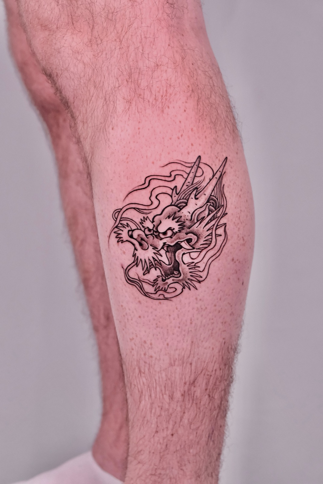 Detailed dragon head tattoo on calf with fine scale detailing