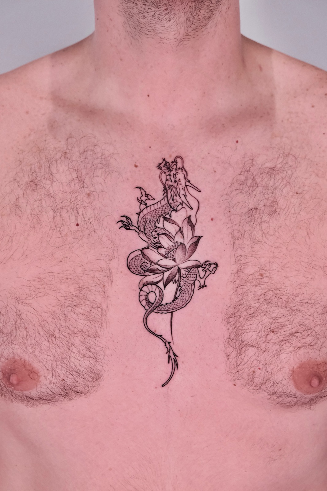 Chinese dragon coiled around a lotus flower tattoo on chest