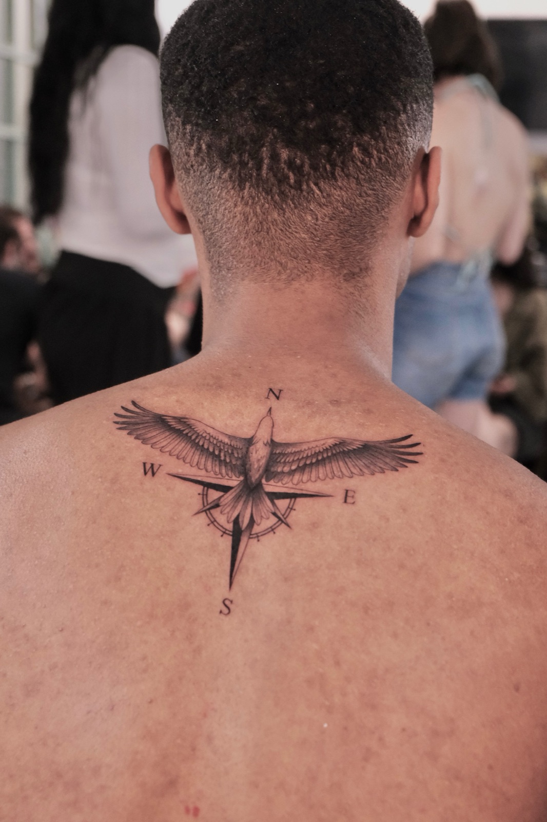 Black-and-grey tattoo of an eagle with spread wings over a compass rose, upper back