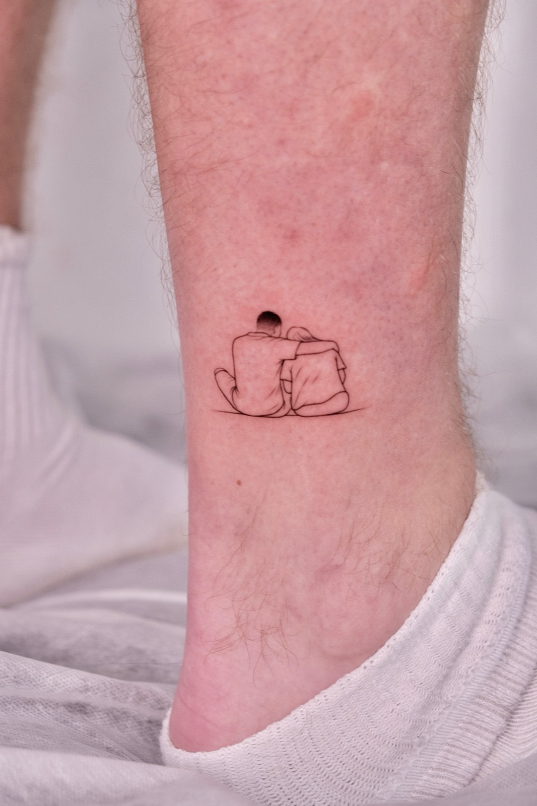 Fine line couple embracing tattoo on the ankle