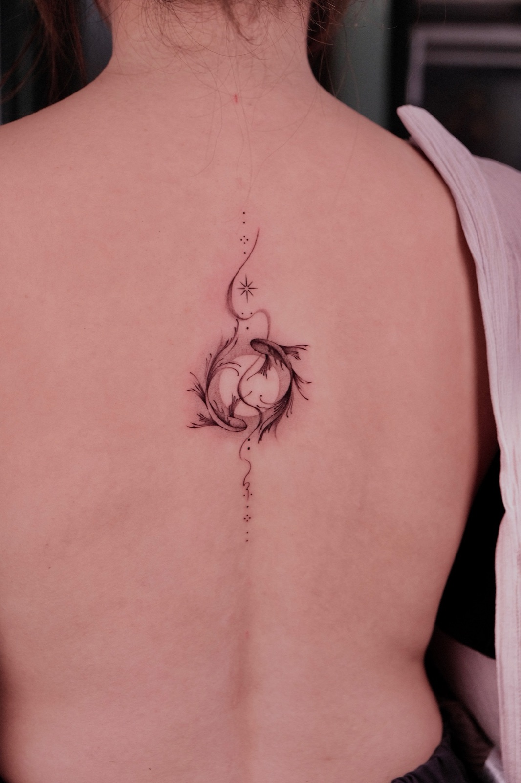 Fine-line dotwork tattoo down the spine combining dragonfly, koi fish, and celestial details