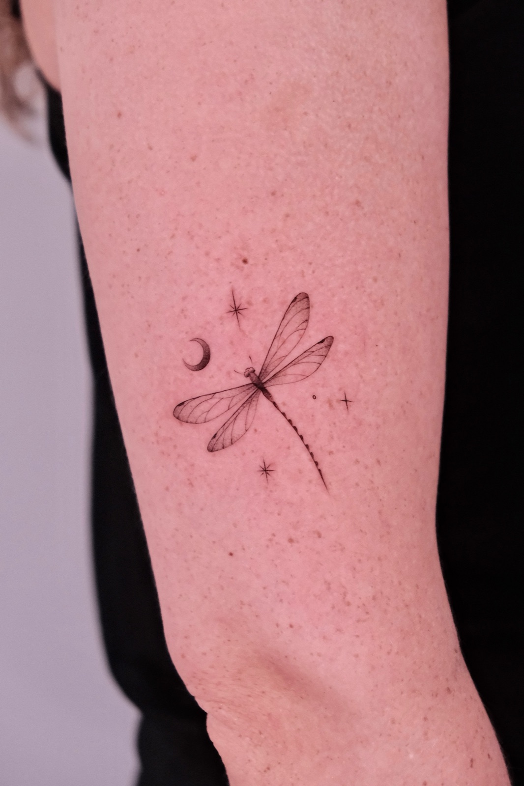 Fine line dragonfly, moon, and star tattoo on the forearm