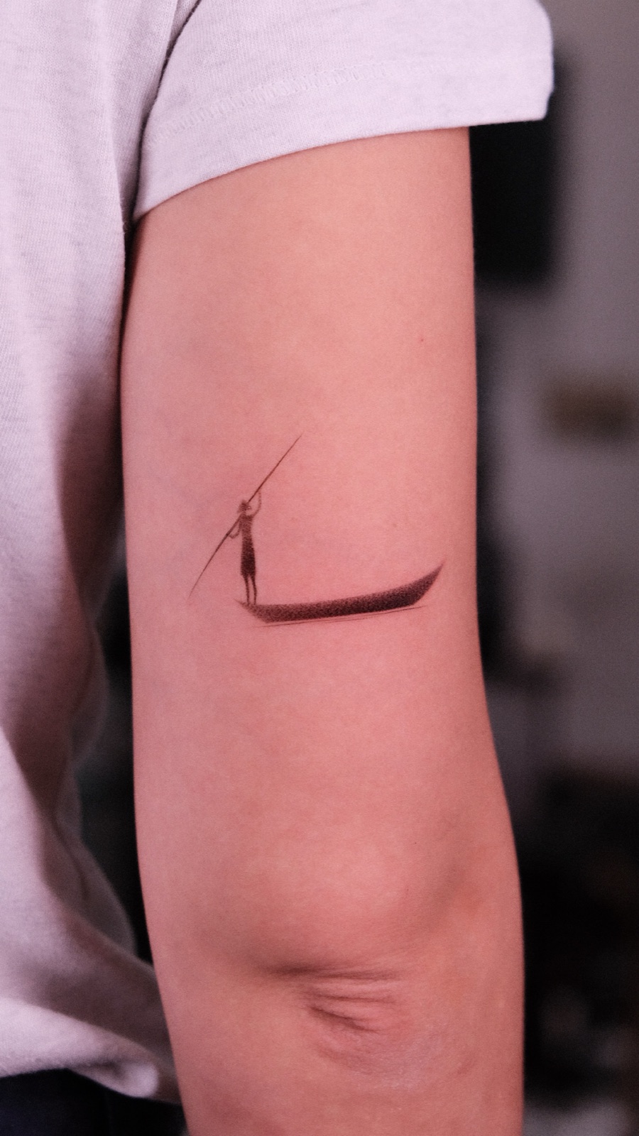 Fine-line silhouette tattoo of a man poling a boat with a long oar