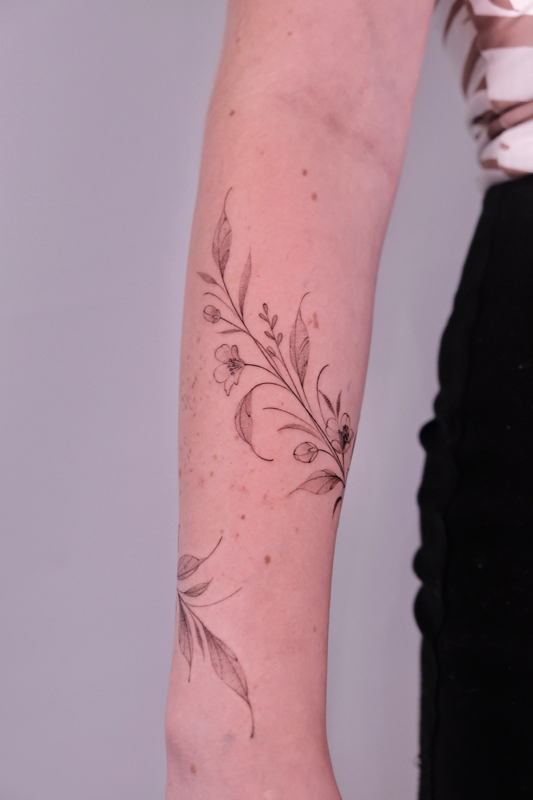 Fine line floral vine tattoo on the forearm, an example of a custom palm-sized design