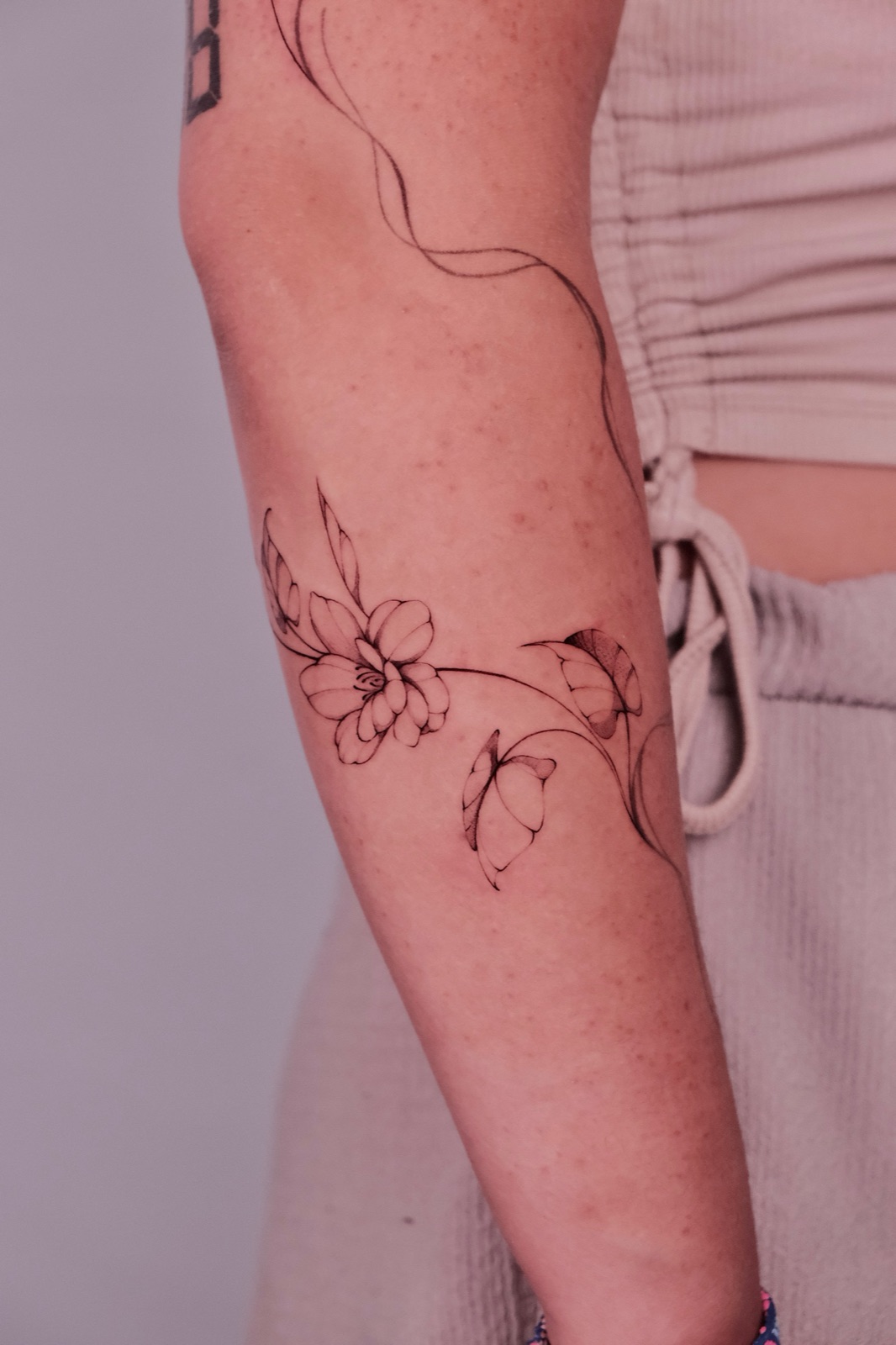 Fine-line flower and butterfly vine tattoo running along the upper arm
