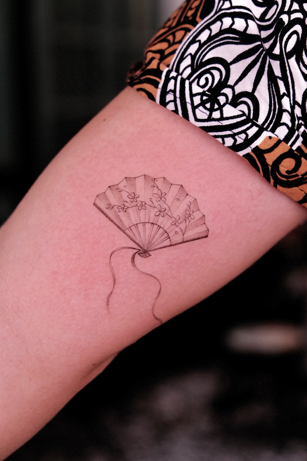 Fine-line folding fan tattoo decorated with cherry blossoms on the forearm