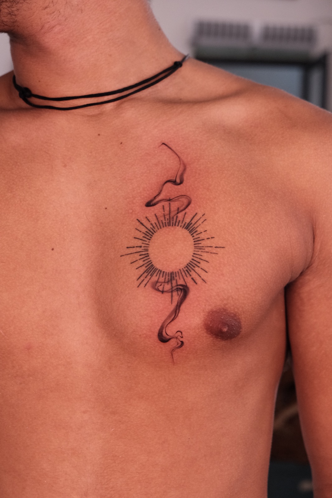 Fine line sunburst tattoo with flowing smoke ribbon on the chest