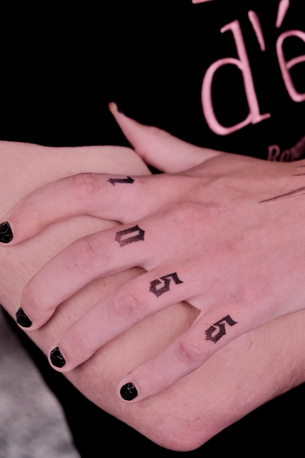 Small number tattoos on each finger spelling out a date, paired with black nail polish