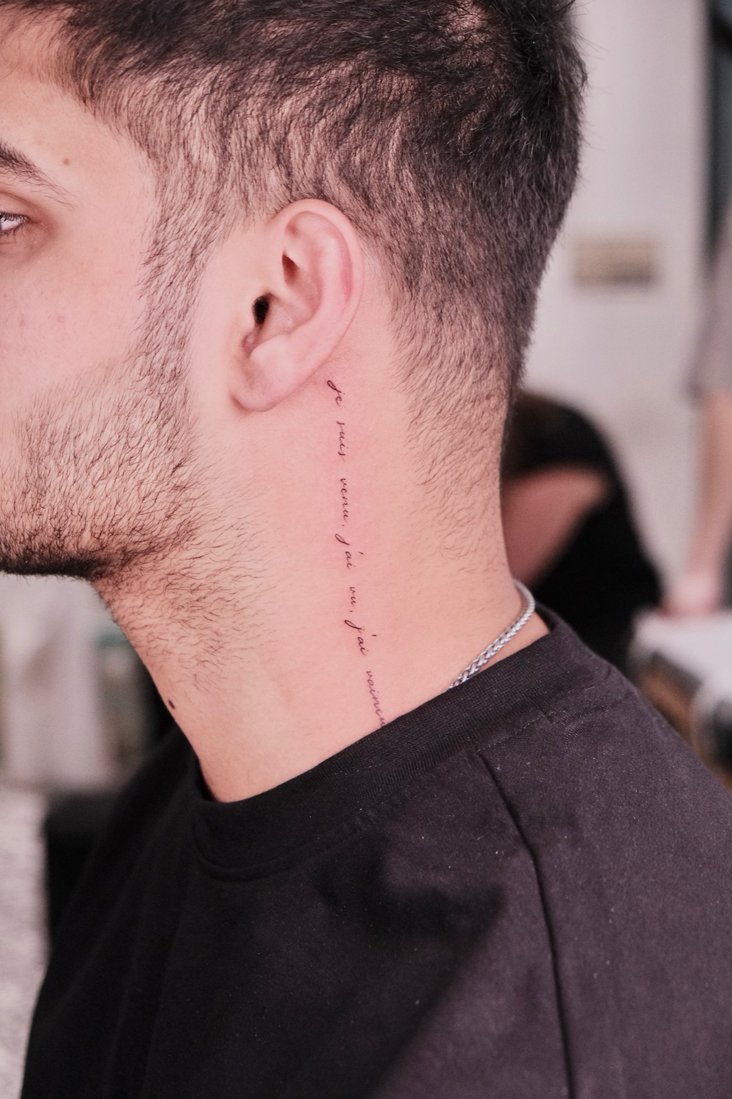 Fine cursive French quote lettering tattoo running down the neck behind the ear