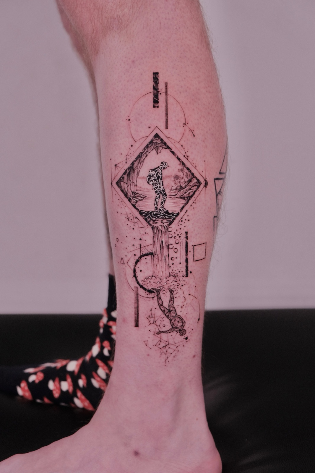 Geometric fine-line tattoo of a mountain climber and waterfall on calf