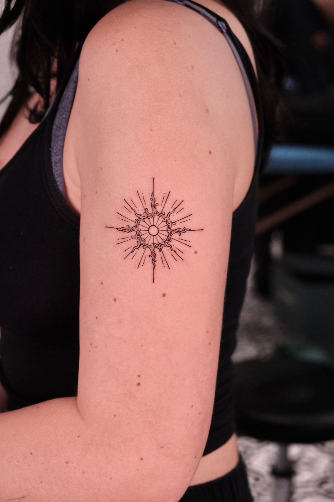 Fine-line radiating sun and mandala geometric tattoo on the upper arm, a symmetrical anchor design used in geometric-themed sleeves