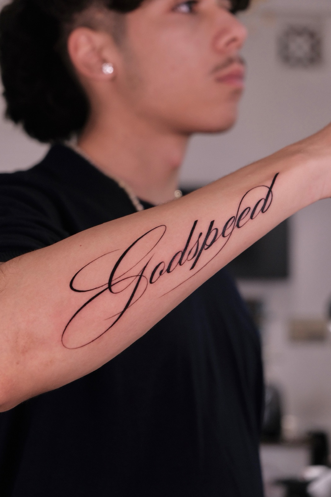 Script lettering tattoo reading Godspeed on the forearm