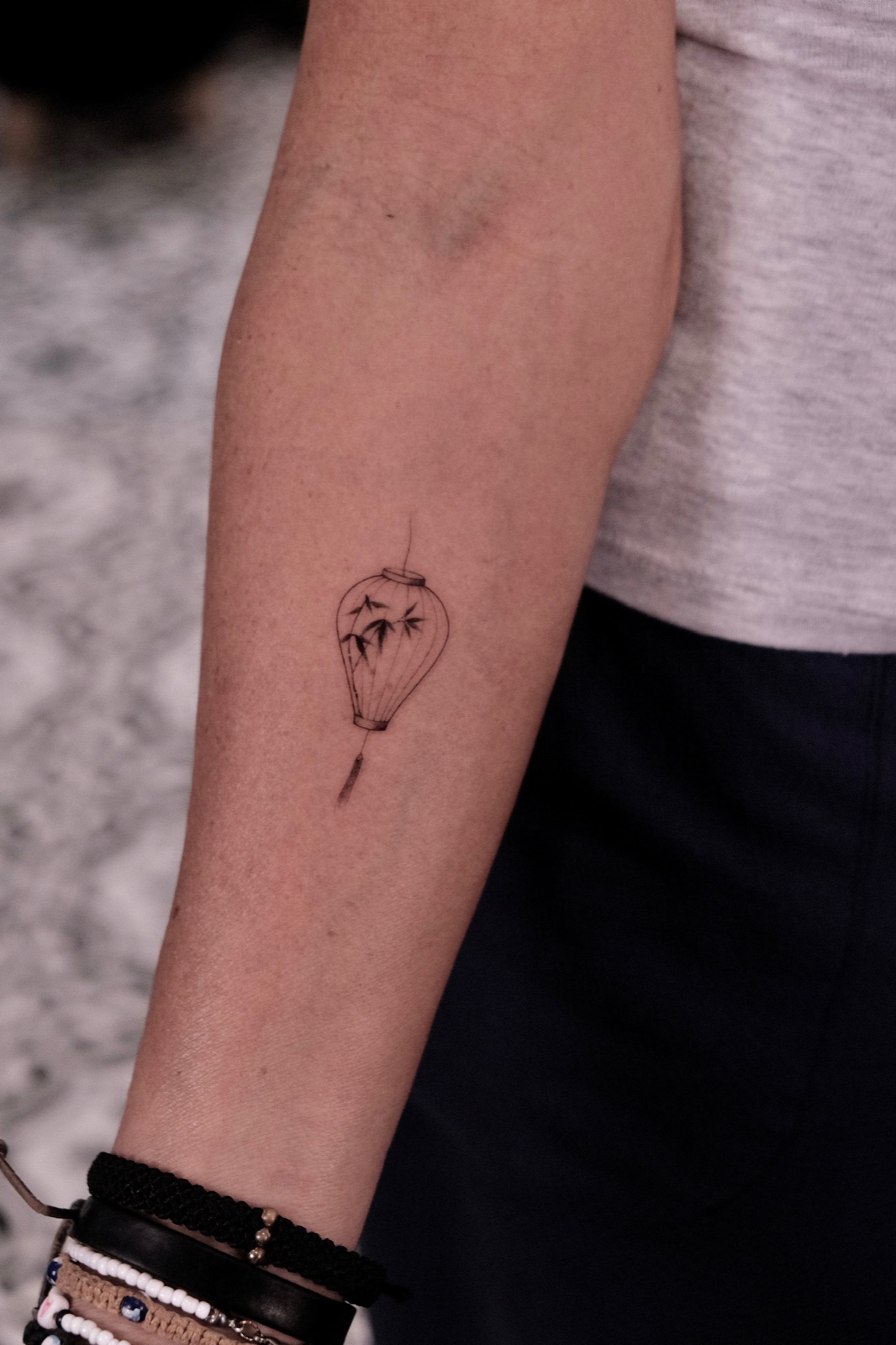 Hanging lantern tattoo with bamboo leaves and a red sun accent on the forearm