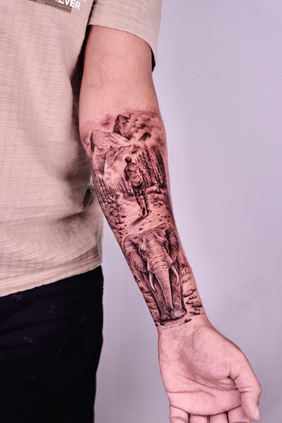 Large black and grey forearm sleeve tattoo of a hiker and an elephant in a mountain landscape, tattooed at Sutran Tattoo Studio