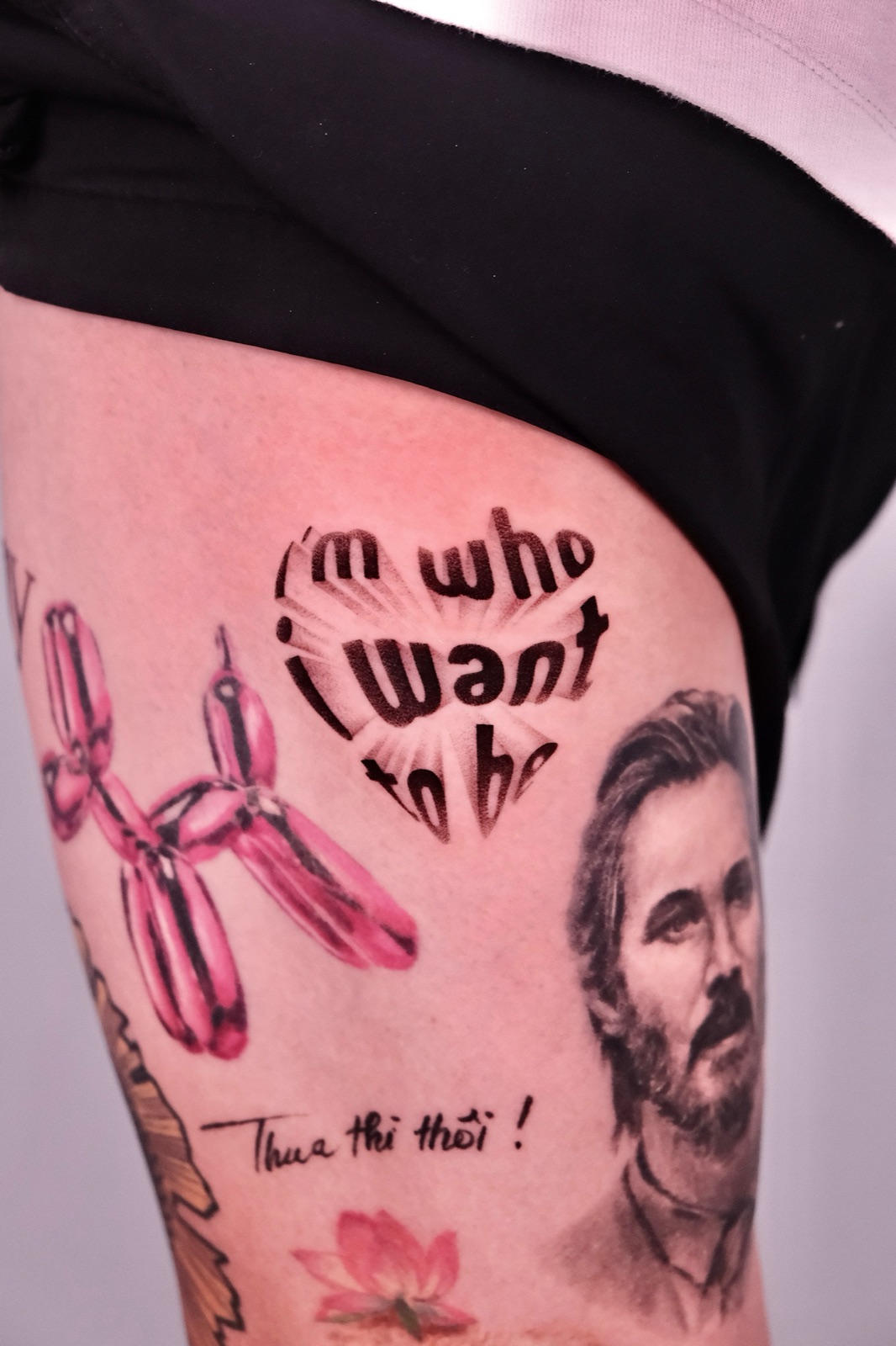 Lettering tattoo reading I'm who I want to be with a balloon dog and portrait on the thigh