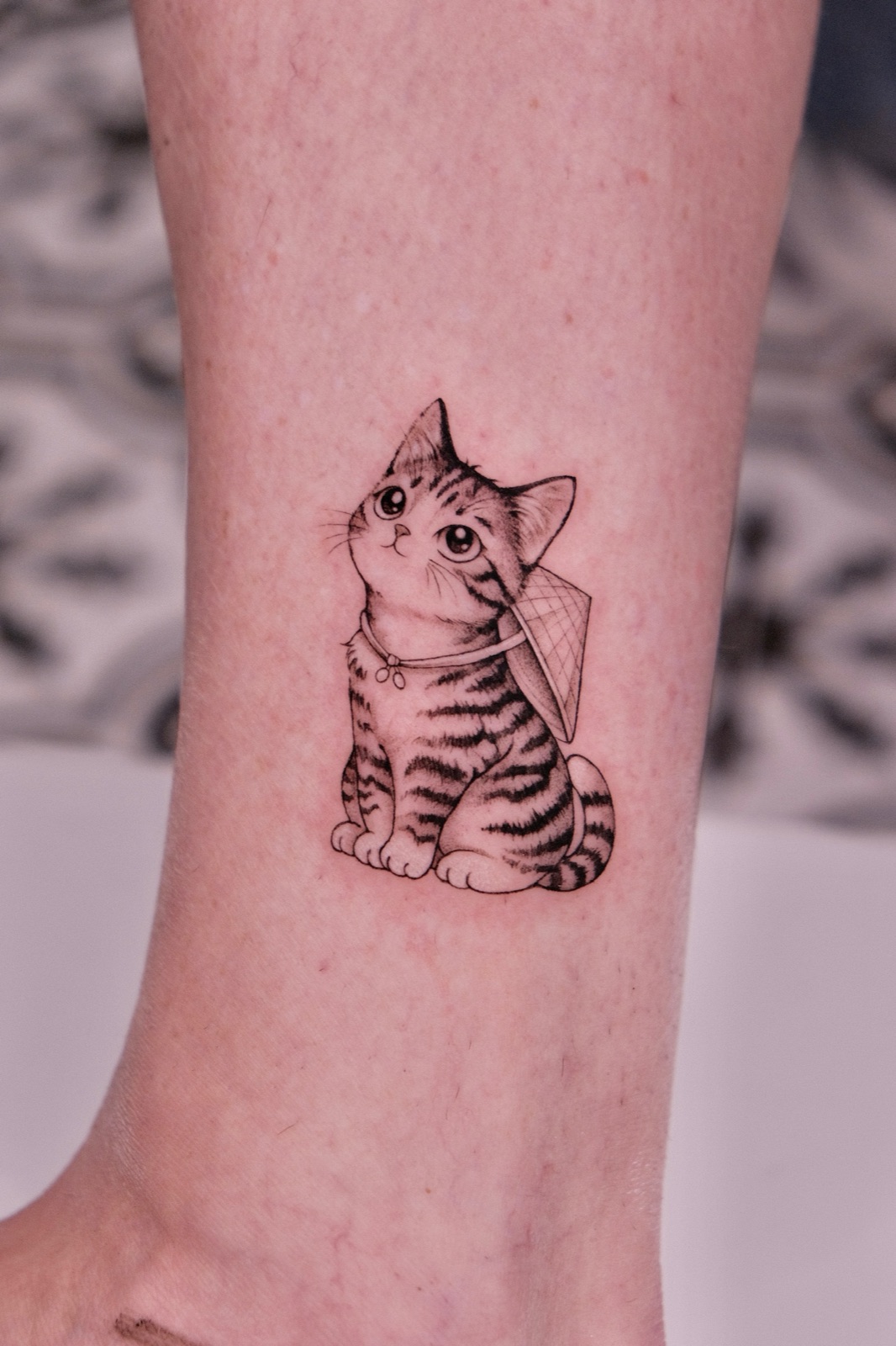 Fine-line tattoo of a kitten wearing a conical hat on the ankle