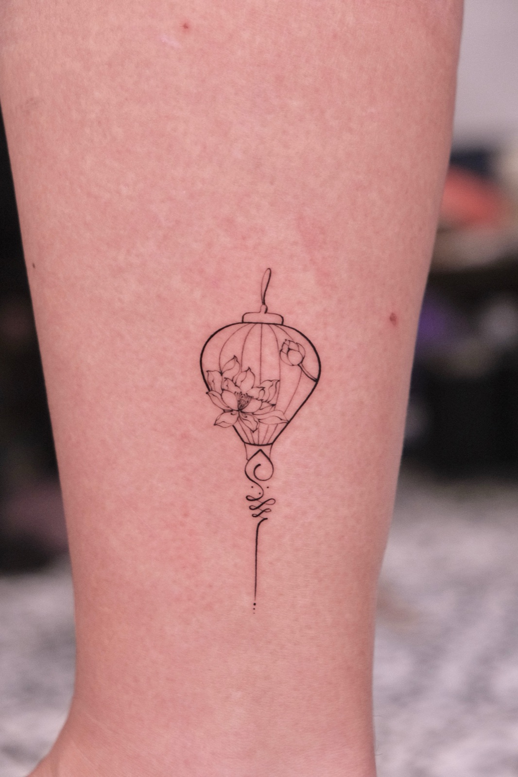 Lantern tattoo with a lotus flower inside trailing into an unalome symbol on the calf