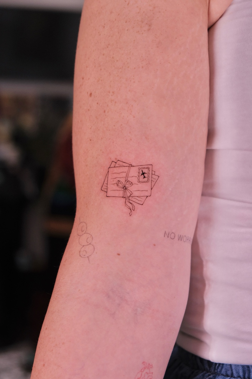Fine-line tattoo of tied letters with an airmail postage stamp on the forearm