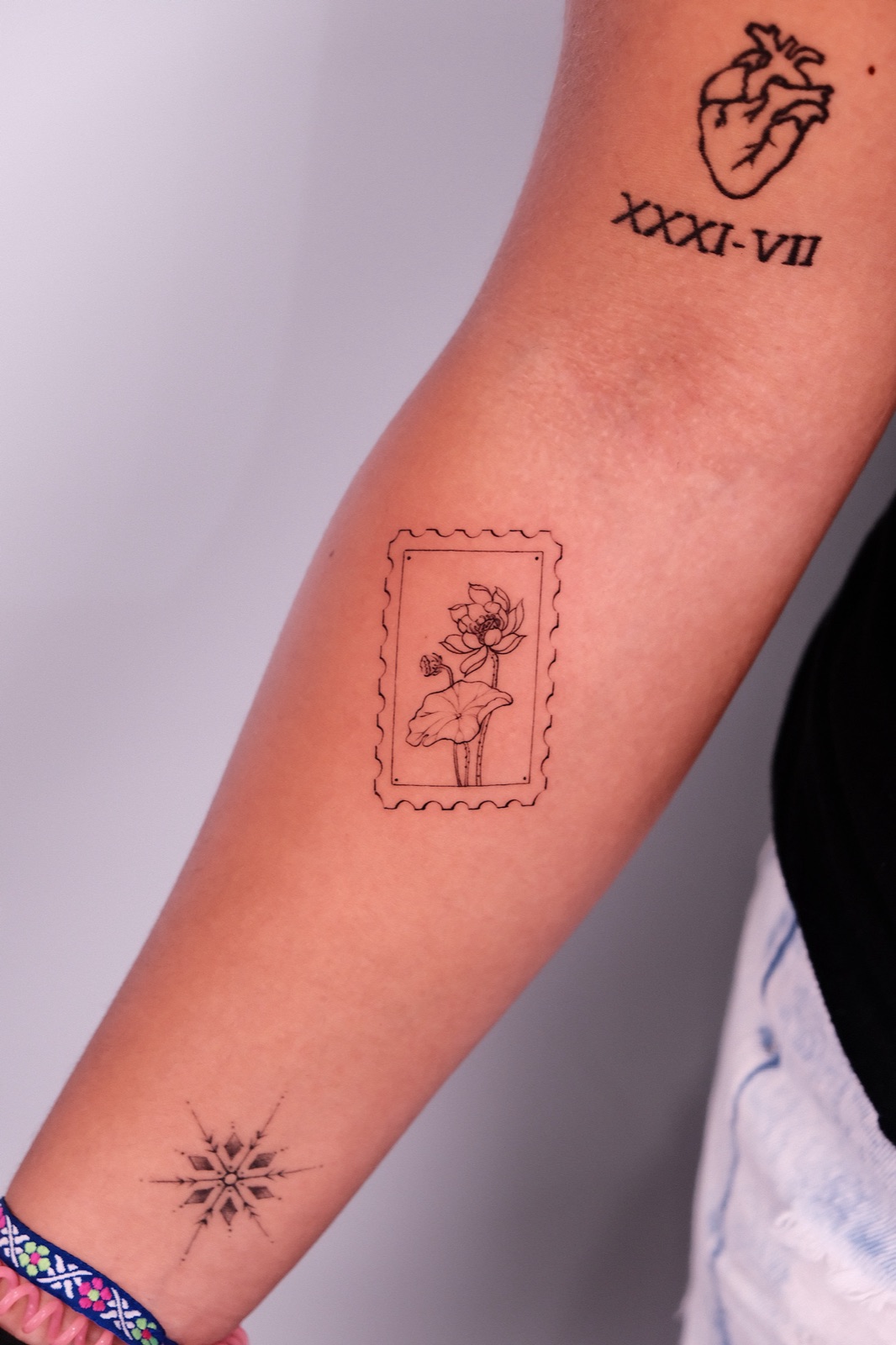 Fine-line lotus flower tattoo designed as a postage stamp on the forearm