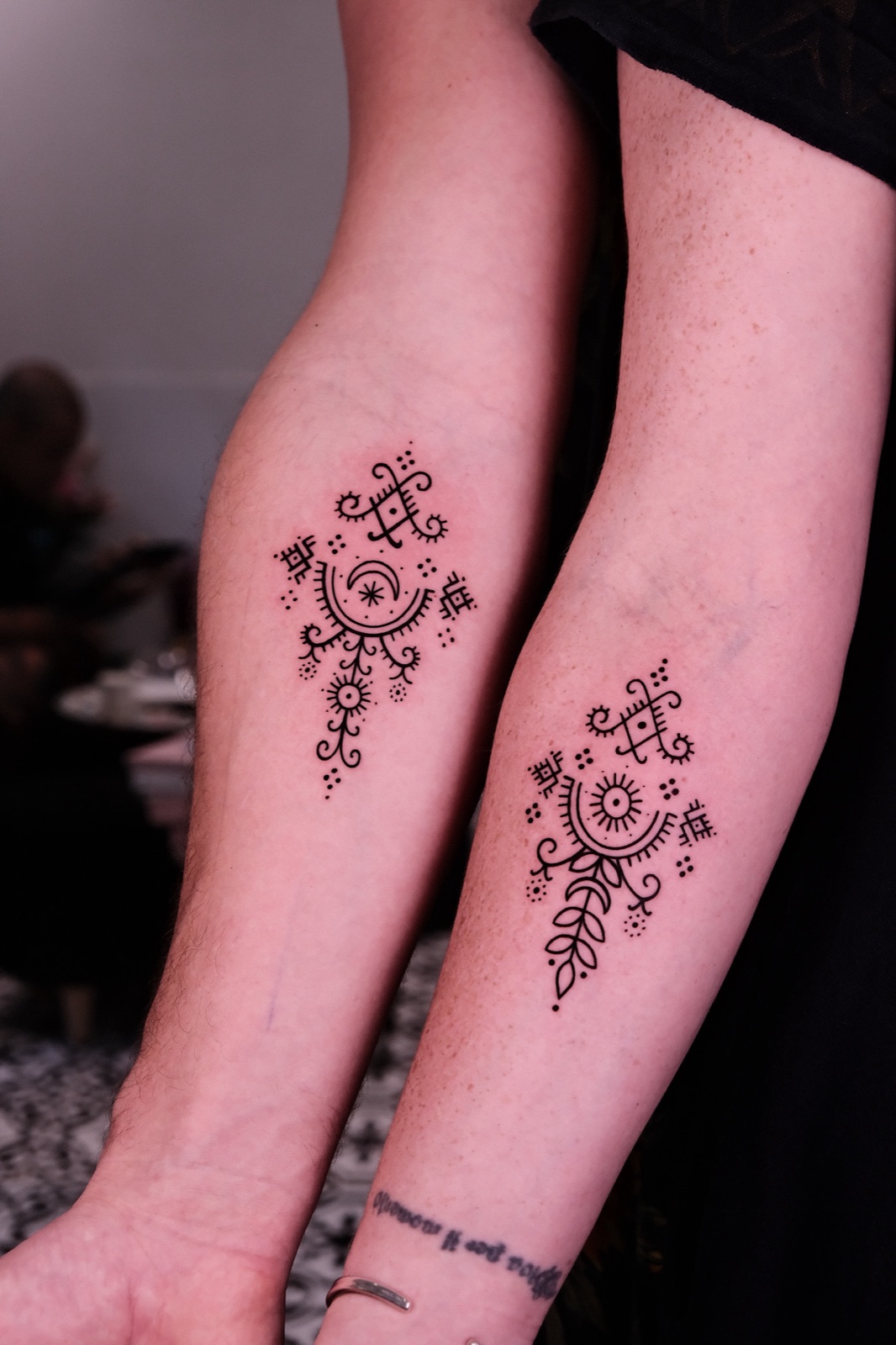 Matching symmetrical ornamental sun and moon fine line tattoos on two forearms