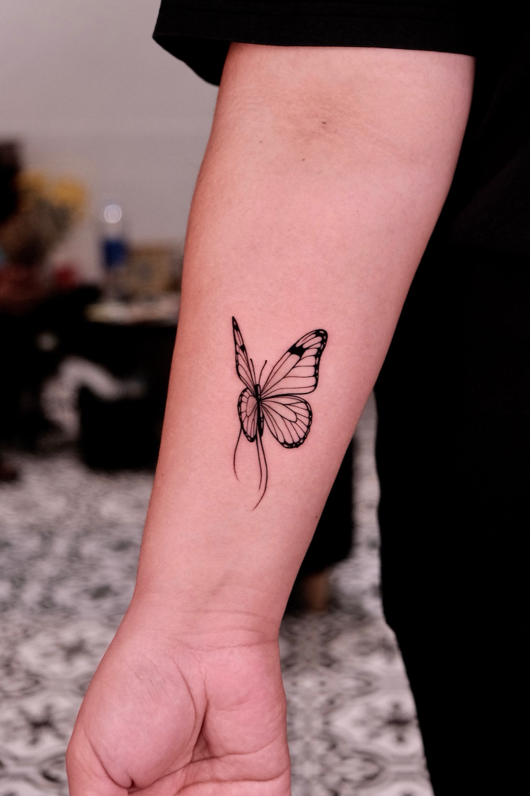 Blackwork monarch butterfly tattoo on forearm near wrist