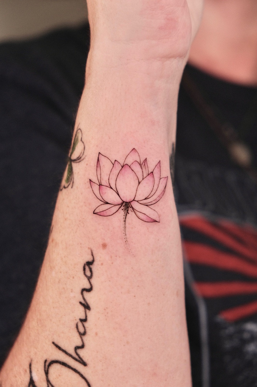 Fine-line lotus flower tattoo with pink watercolor wash on the wrist