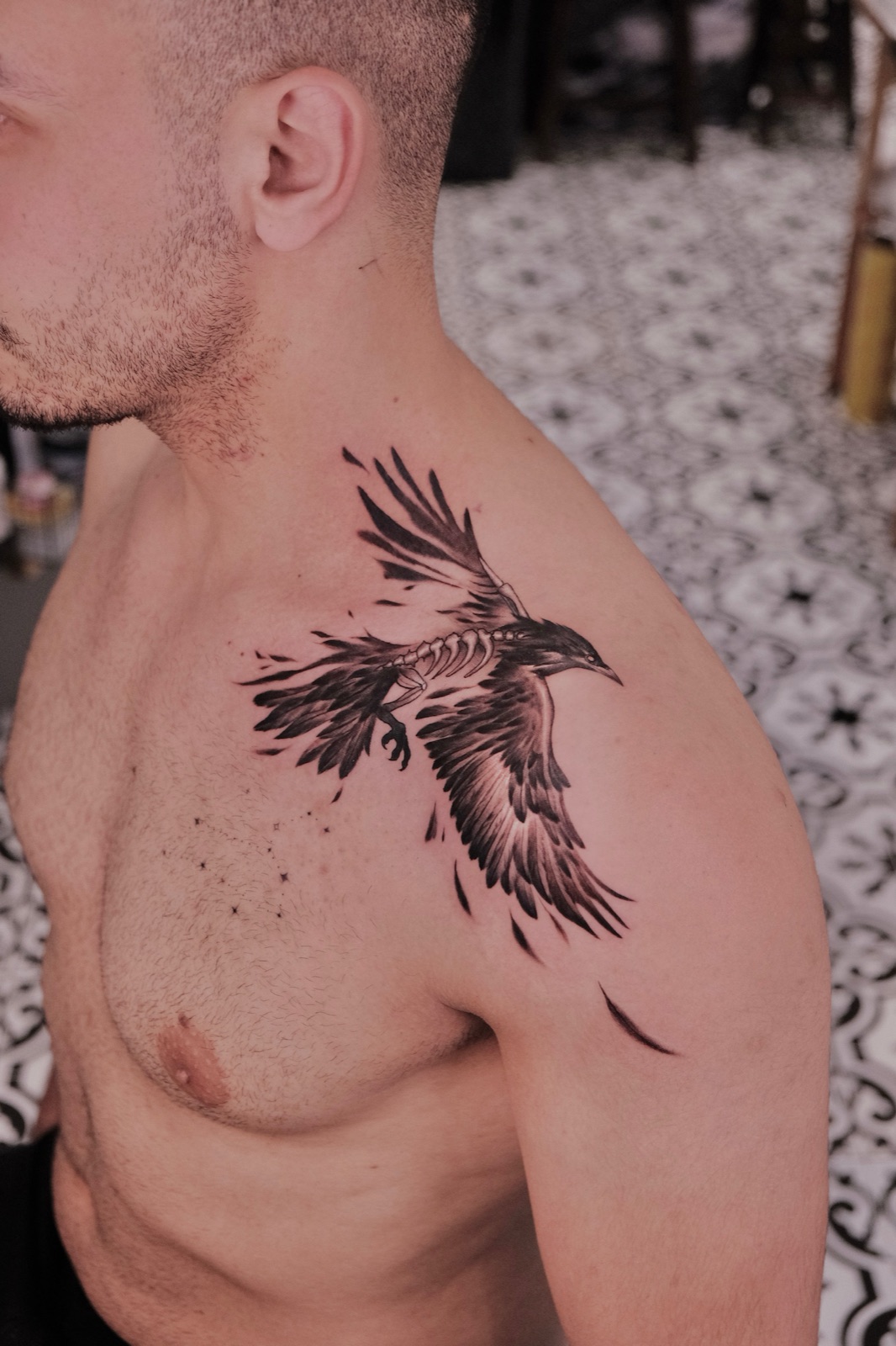Black and grey raven skeleton wing tattoo spread across the chest and shoulder
