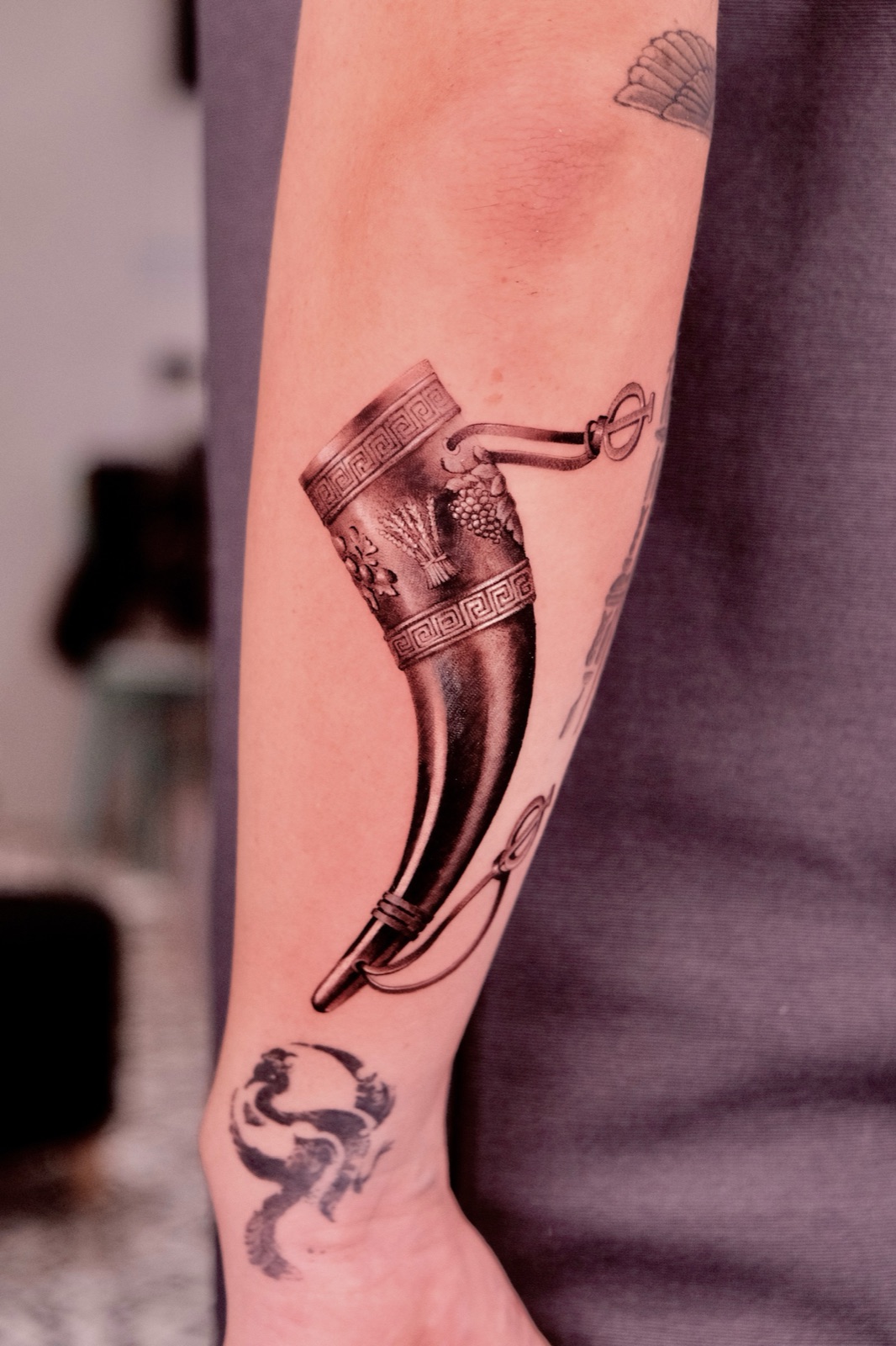 Realistic black and grey tattoo of an ornate drinking horn on forearm