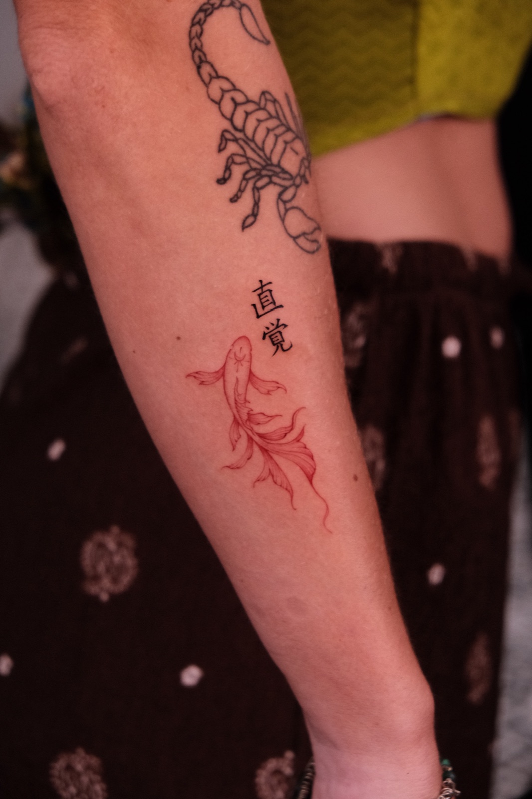 Fine-line red koi fish tattoo beneath vertical kanji lettering on the forearm