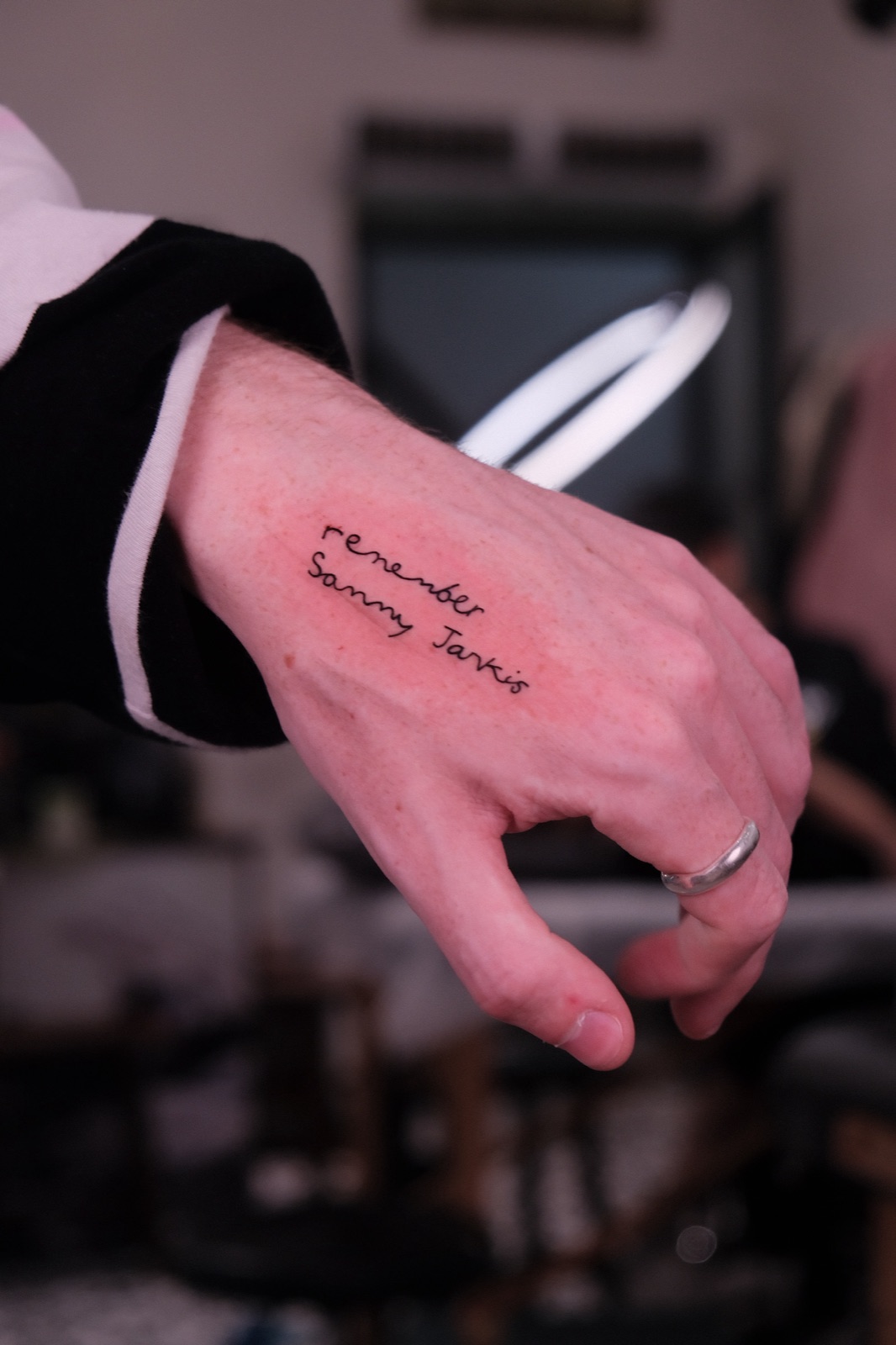 Small handwritten lettering tattoo reading remember Sonny Jarkis on the back of the hand