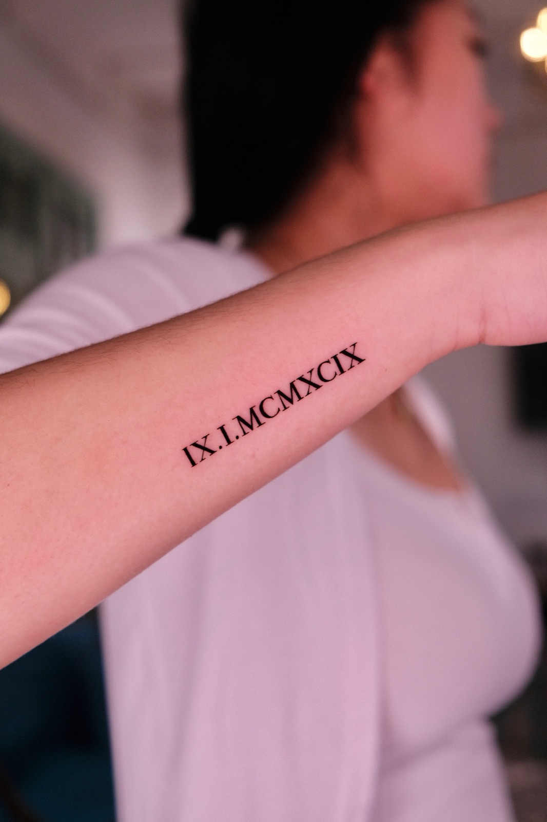 Roman numeral date tattoo in serif lettering on the inner forearm