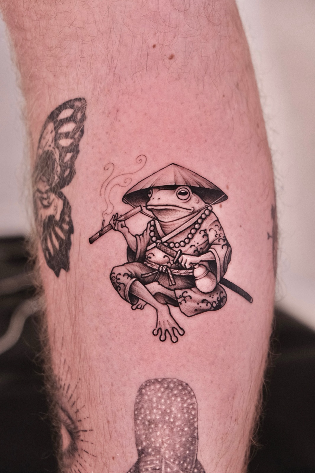 Neo-traditional tattoo of a samurai frog smoking a pipe on a client's calf