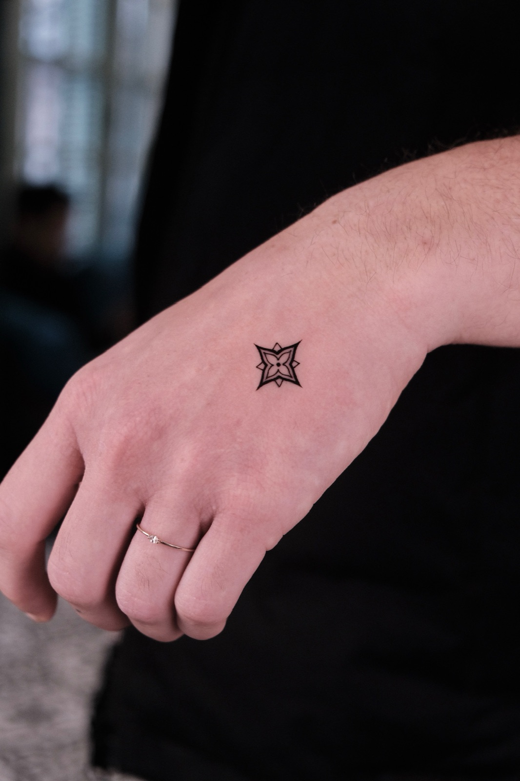 Small blackwork star-flower tattoo on the back of a hand near the wrist