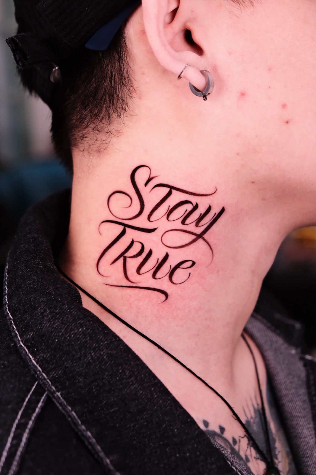 Script lettering tattoo reading Stay True on the side of the neck