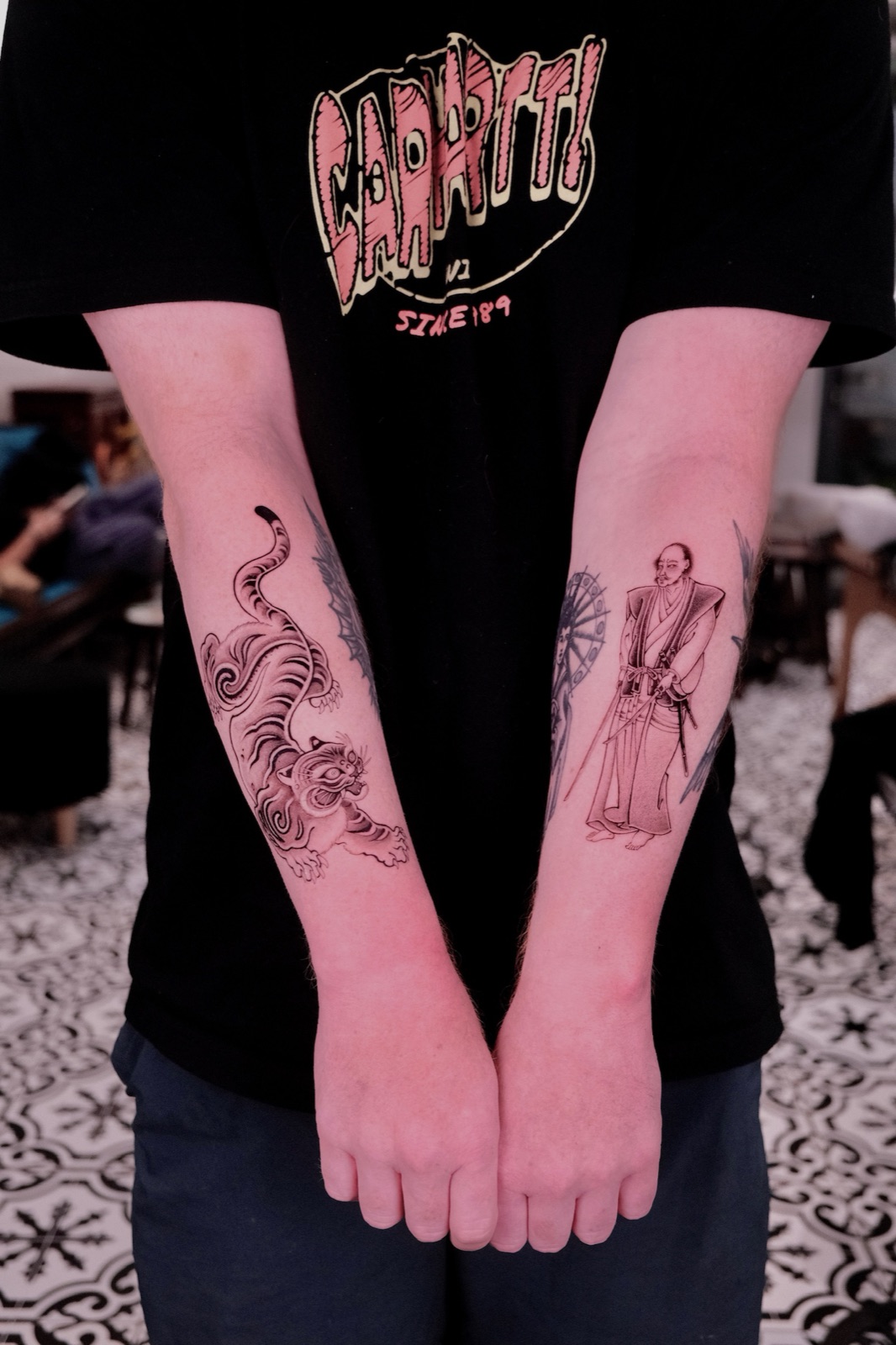 Matching tiger and samurai figure forearm tattoos on two arms