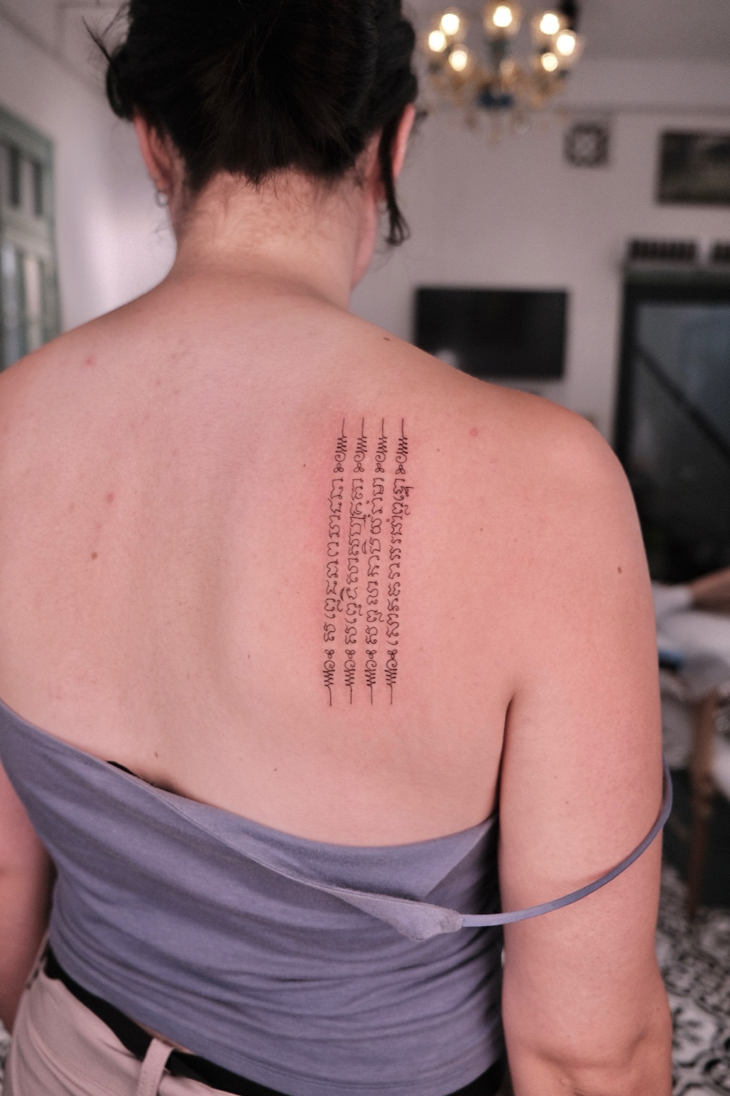 Ornamental script tattoo running in vertical columns down the upper back