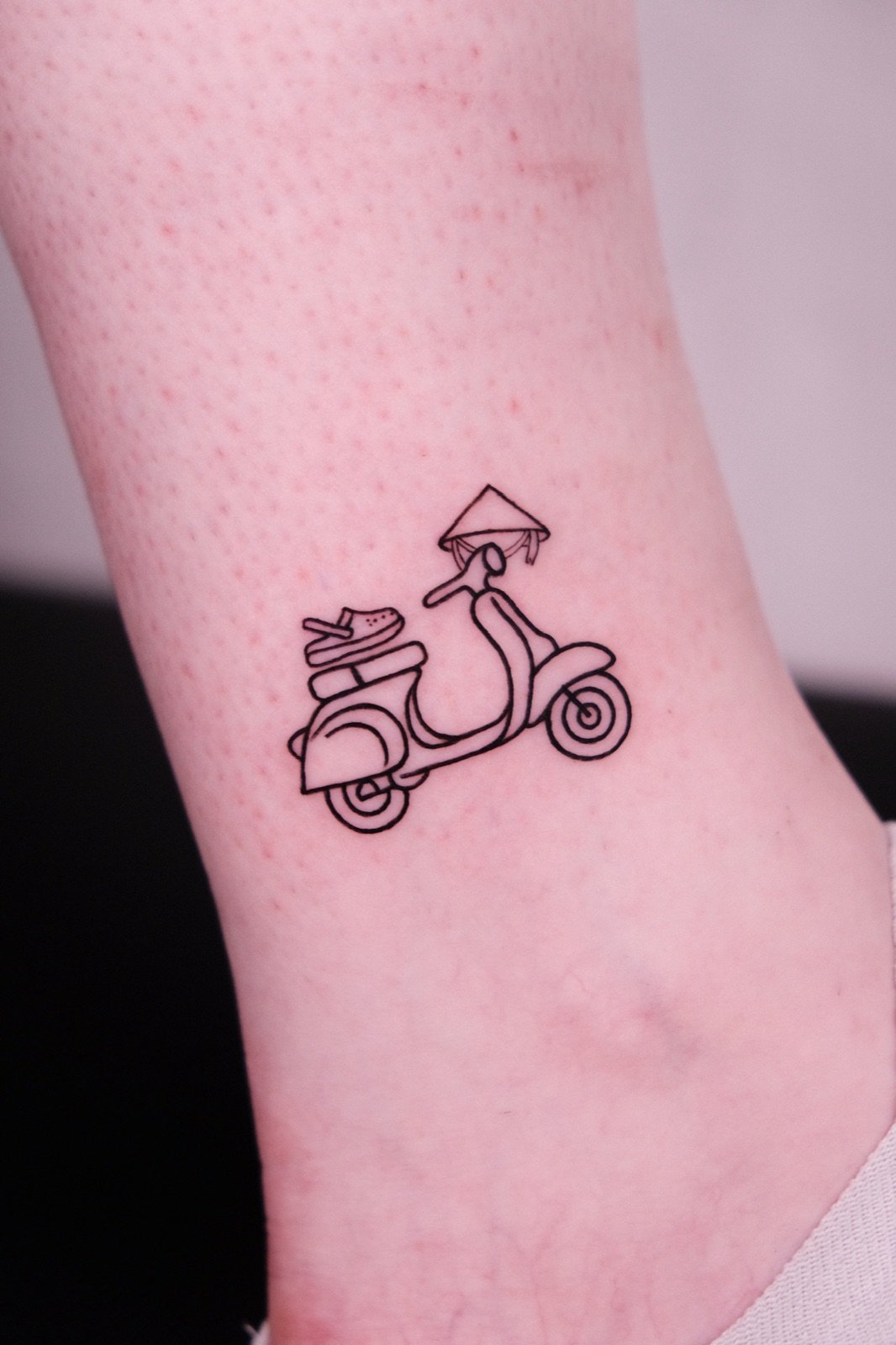 Fine-line Vespa scooter tattoo with a Vietnamese conical hat on the ankle