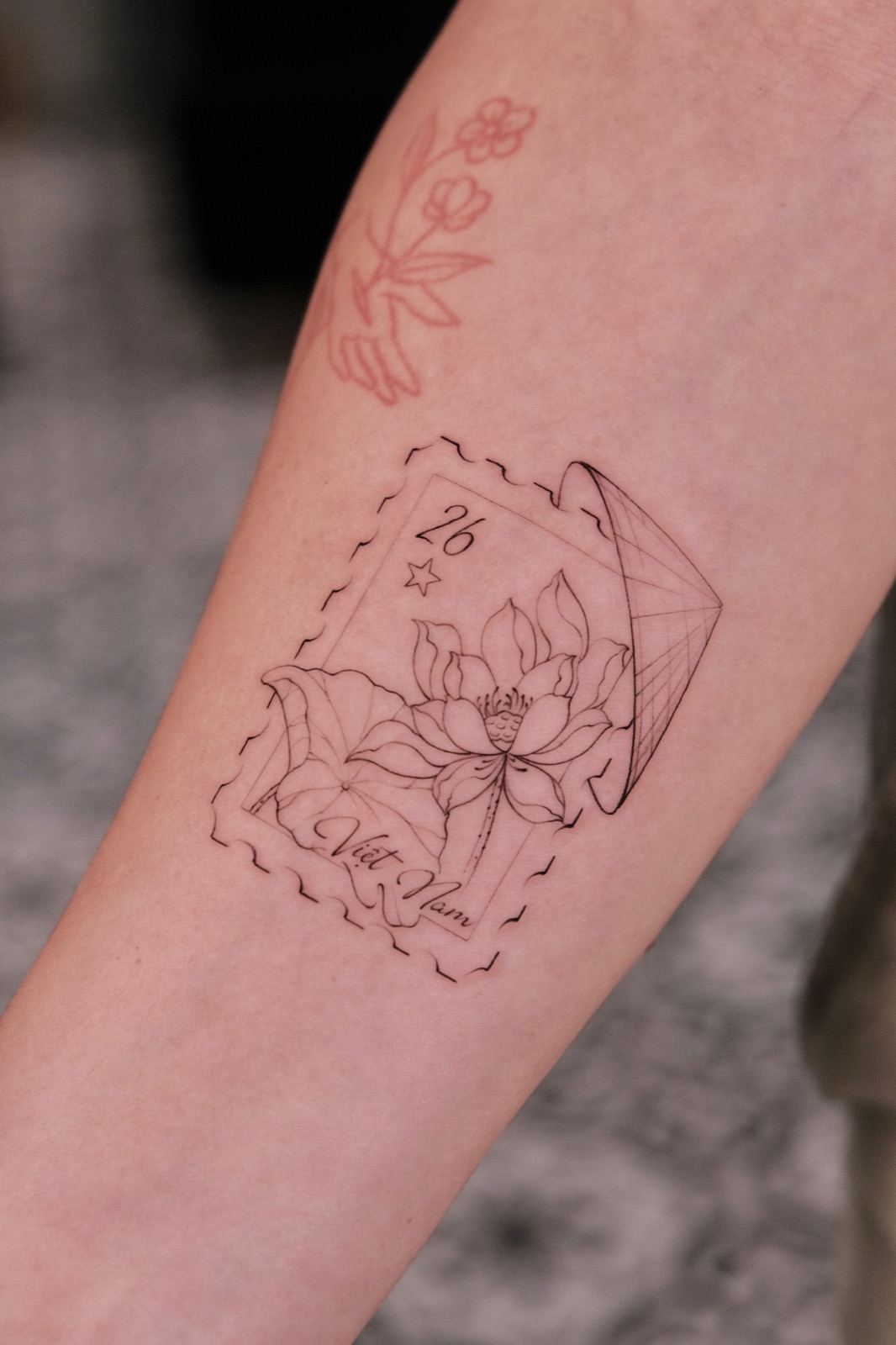 Fine-line Vietnam postage stamp tattoo featuring a lotus flower and conical hat on the forearm