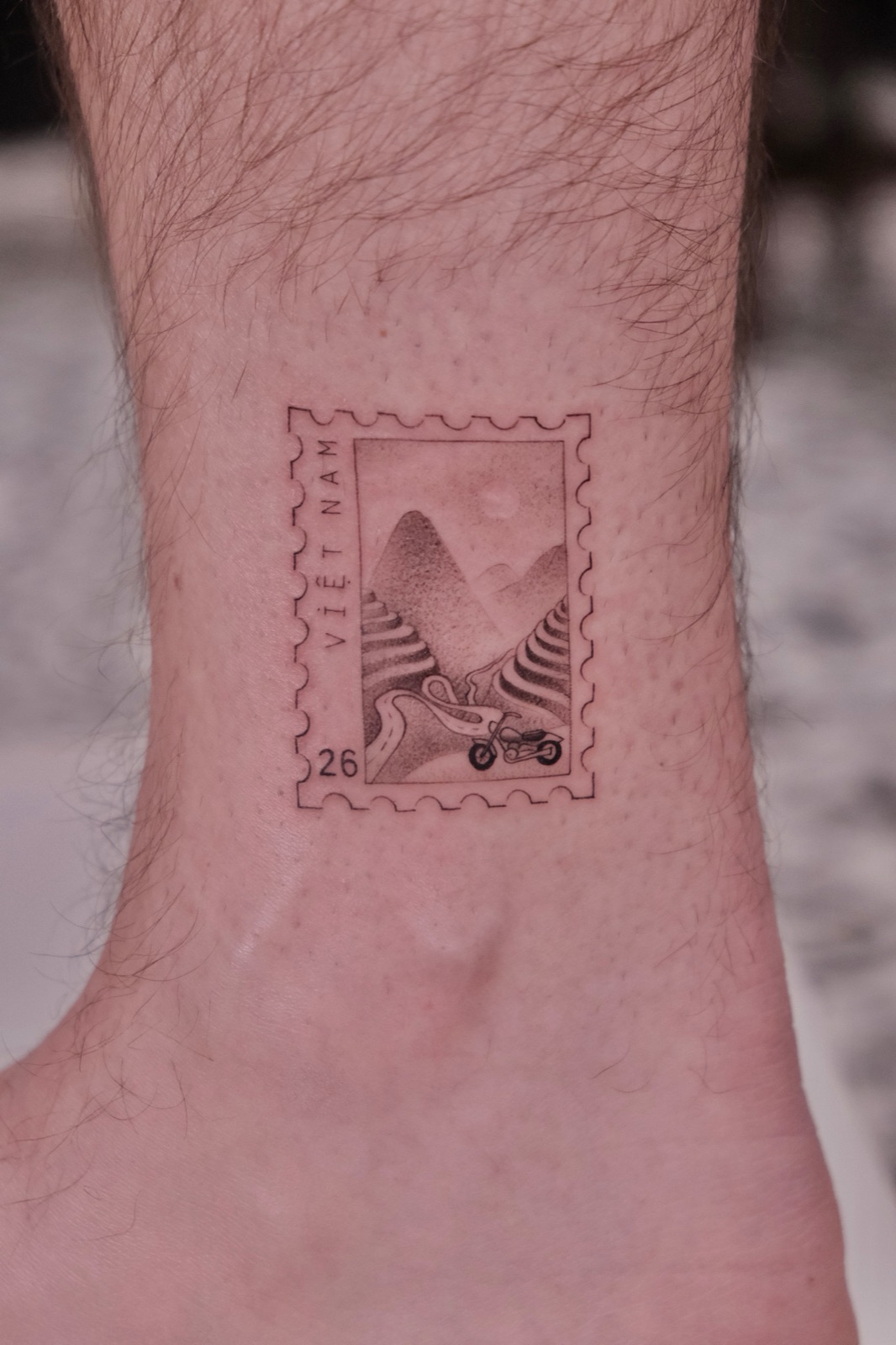 Vietnam postage stamp tattoo of a motorbike on a mountain road, on the ankle